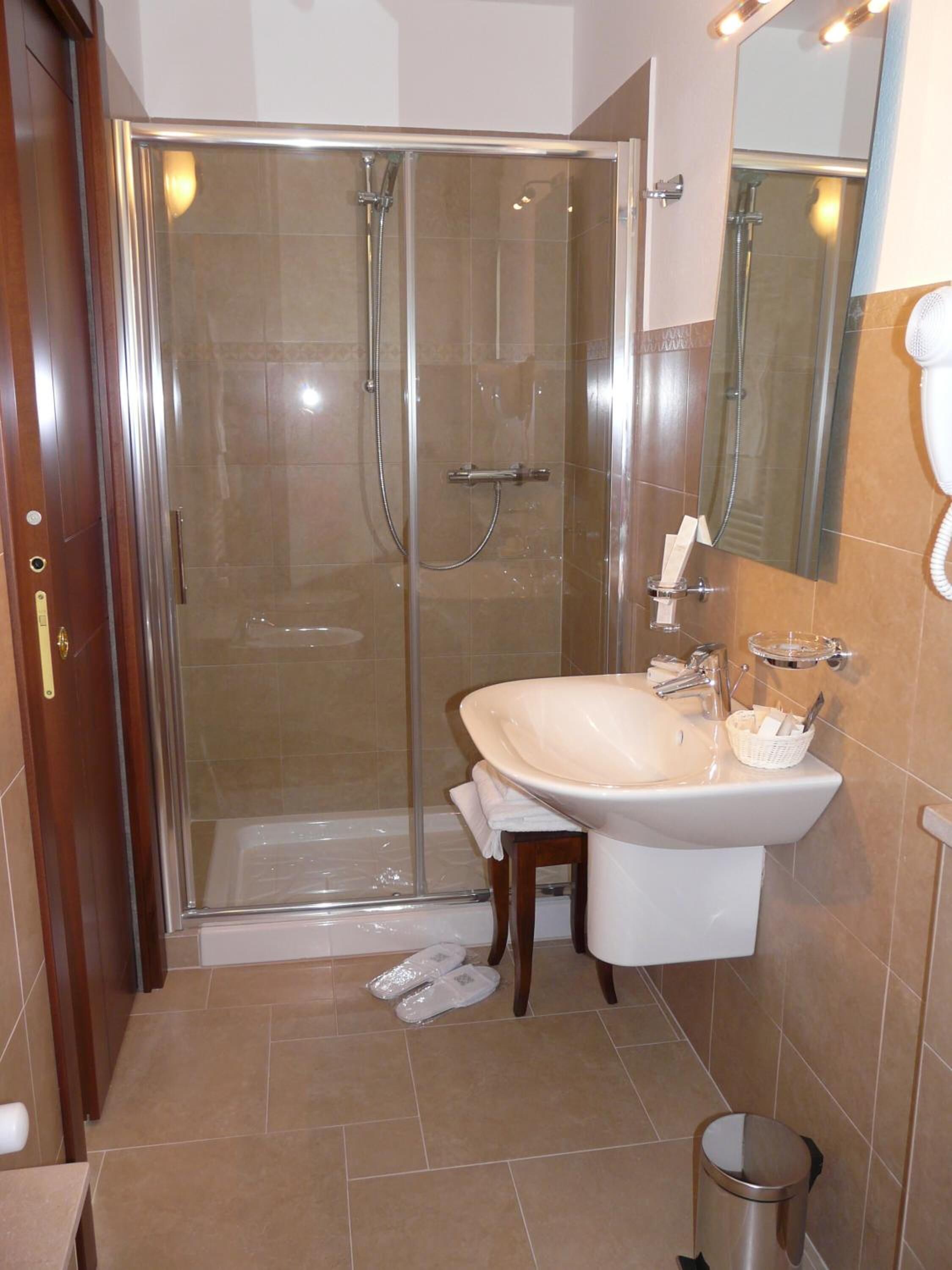 A modern bathroom with a glass-enclosed shower, a white sink with a mirror, and a trash can.