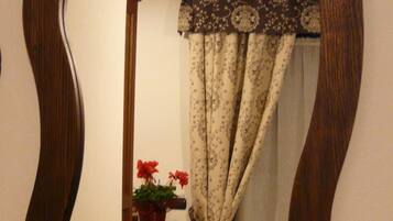 A mirror with a wavy frame reflecting a bathroom with a patterned curtain, a potted plant, and a small table.