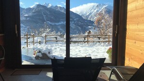 A room with a large sliding glass door leading to a snowy outdoor area with a wooden fence and a chair. - B&B Verger Plein Soleil (Saint-Pierre)