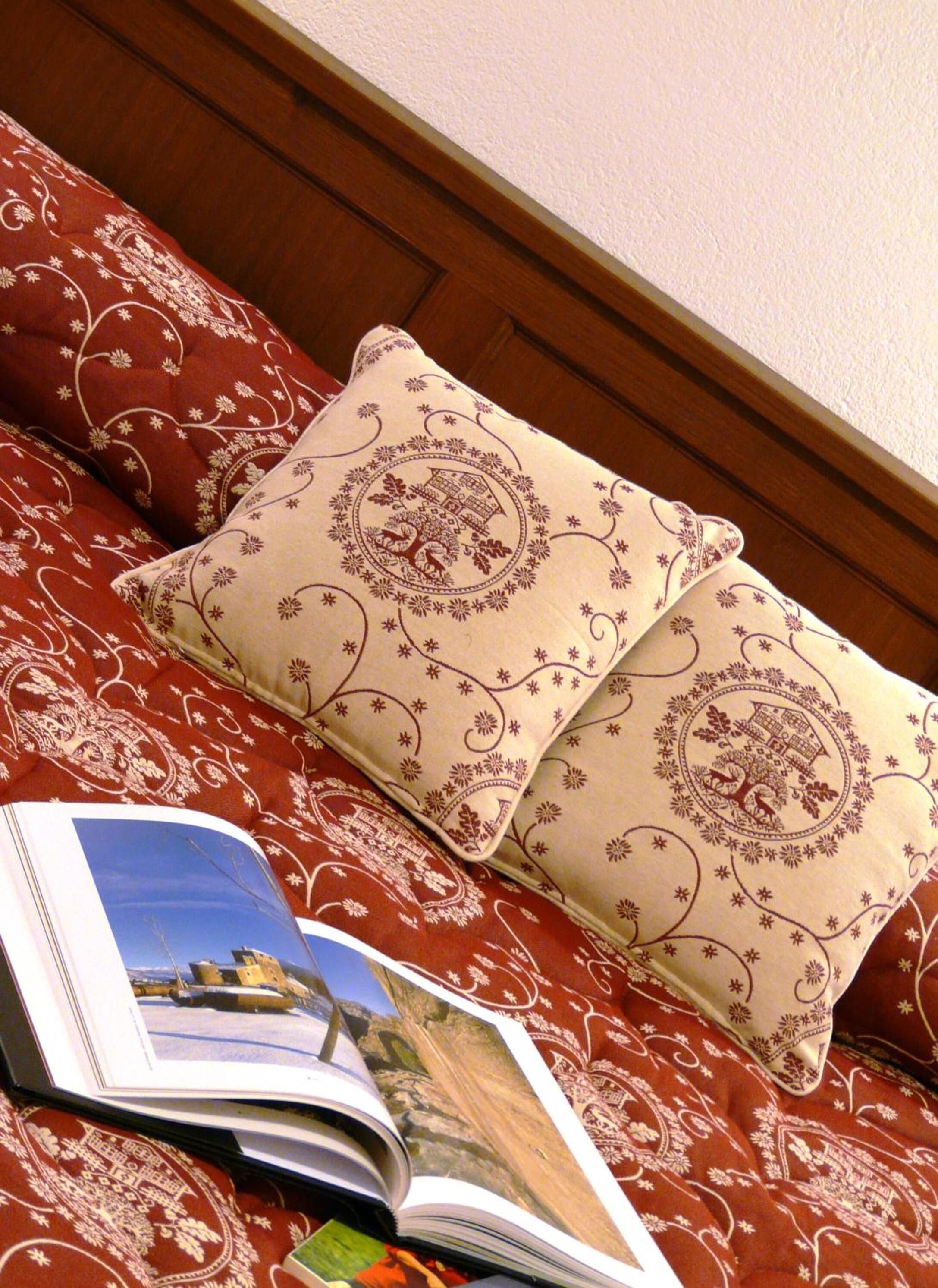 A bed with red bedding and two decorative pillows with a paisley pattern.