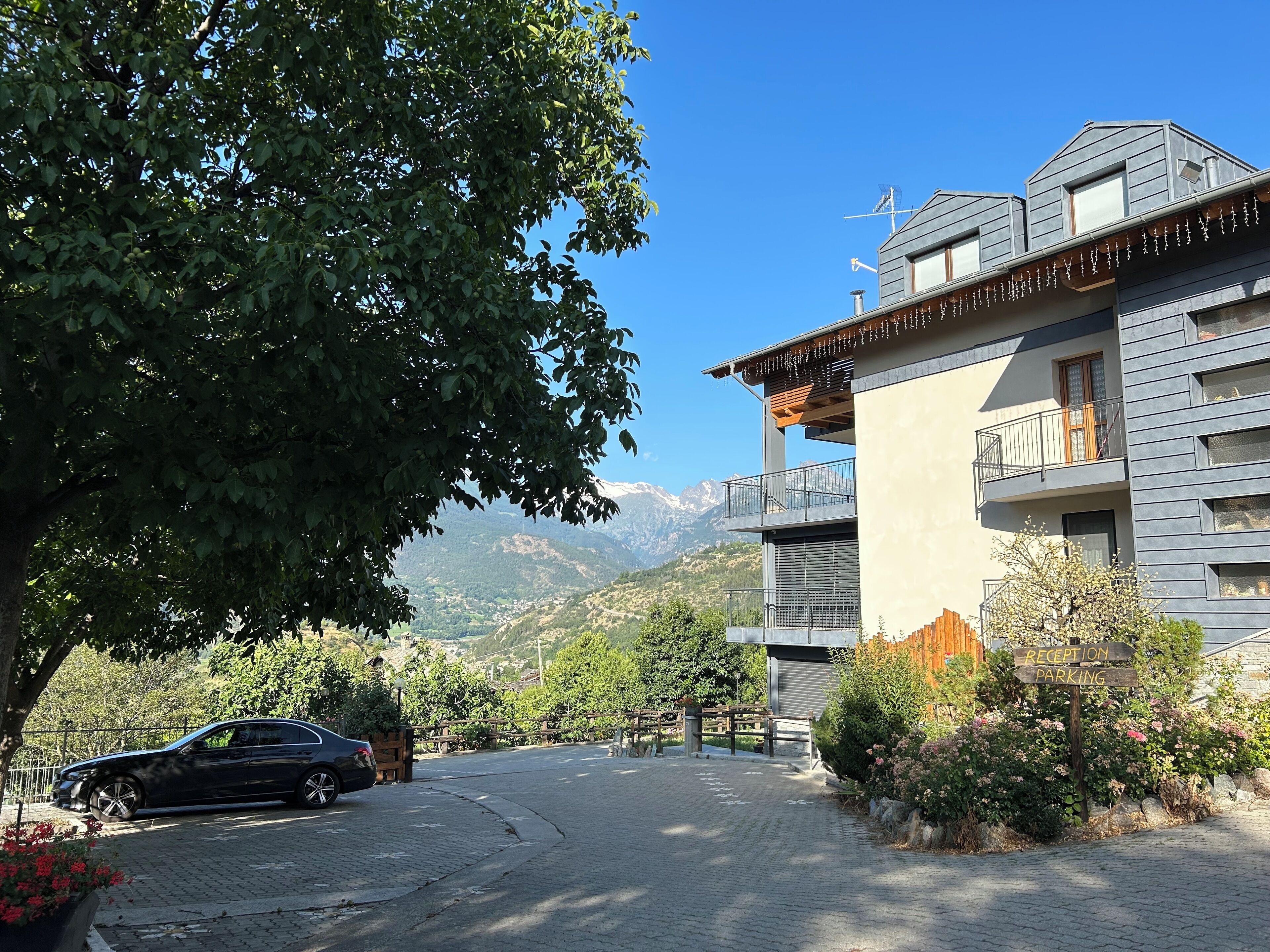 A modern building with a reception area, a parked car, and a mountainous backdrop.