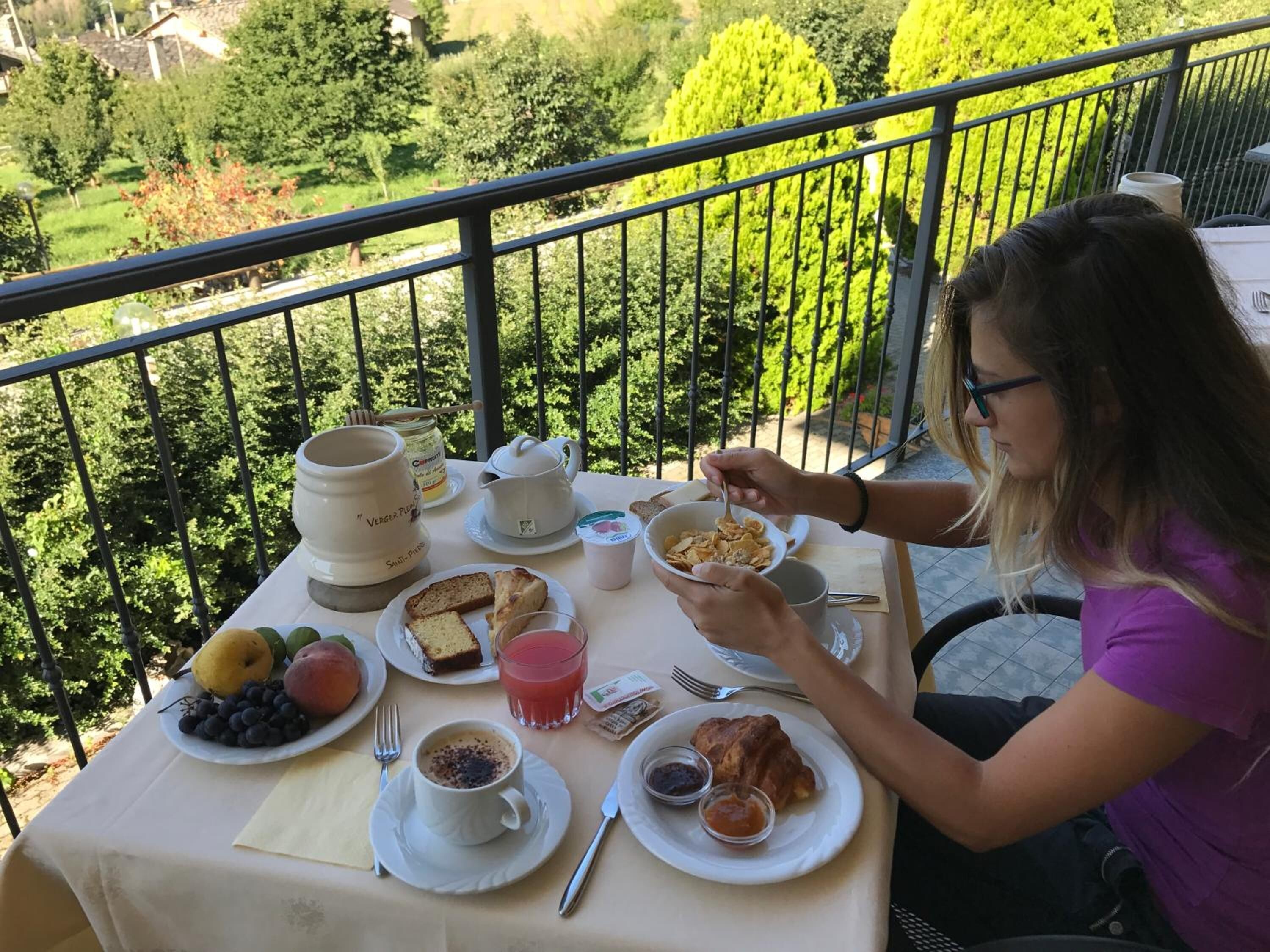 A balcony table with breakfast items including bread, fruit, and coffee.