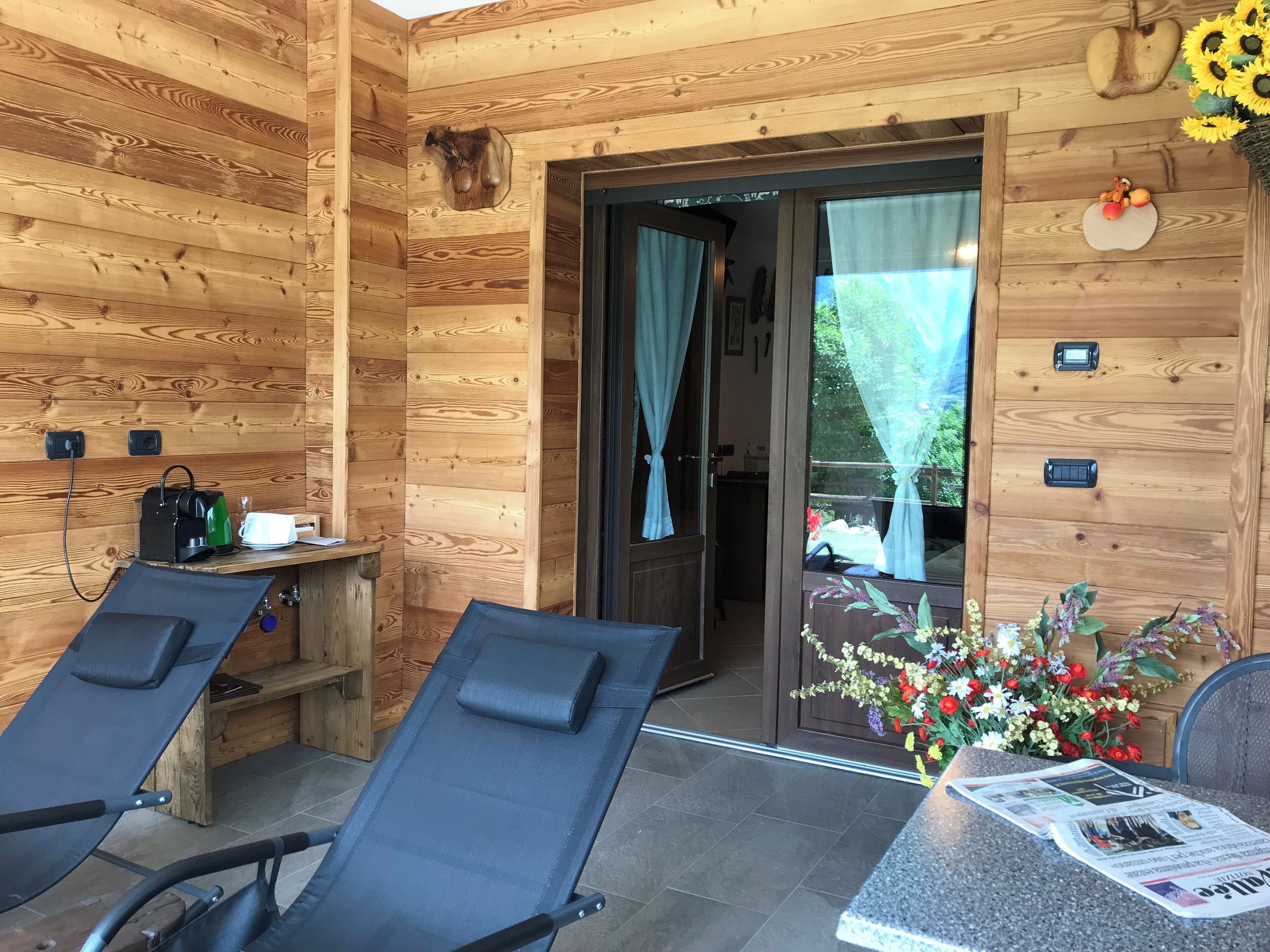 A wooden cabin with two reclining chairs, a small table with a newspaper, and a door leading outside.