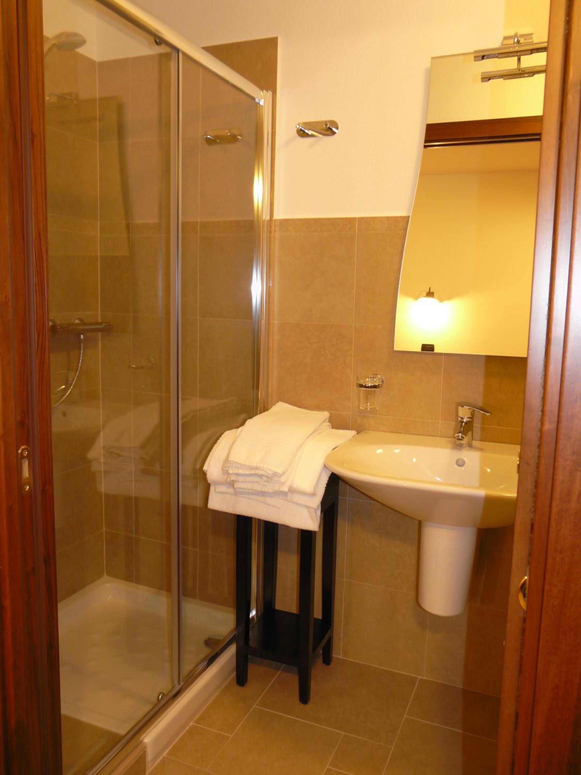 Un bany amb plat de dutxa de vidre, un lavabo amb mirall i un escurapins.