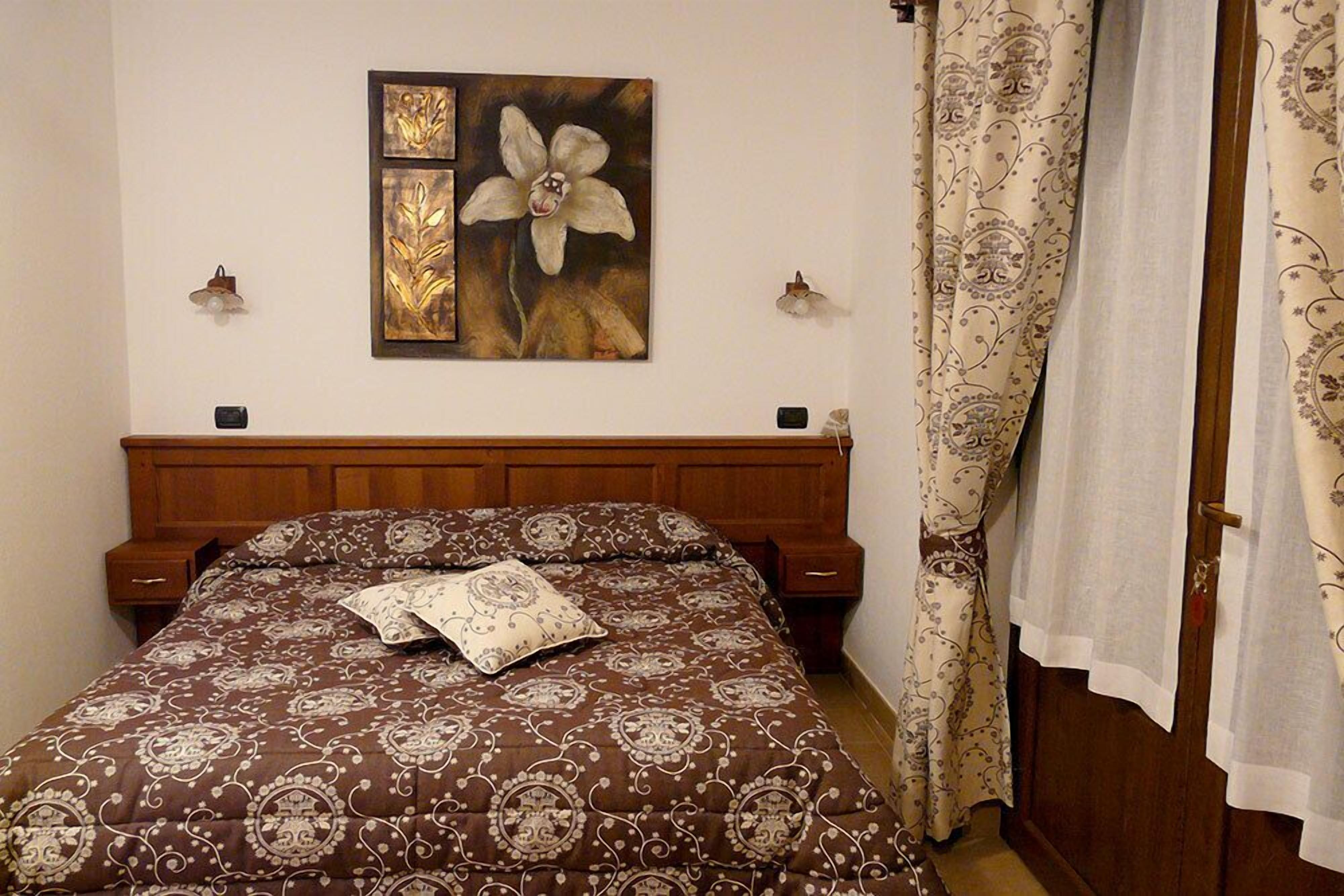 Ein Schlafzimmer mit einem Holz-Kopfteil, einer gemusterten Bettdecke, einem Kopfkissen und einem Blumenbild an der Wand.