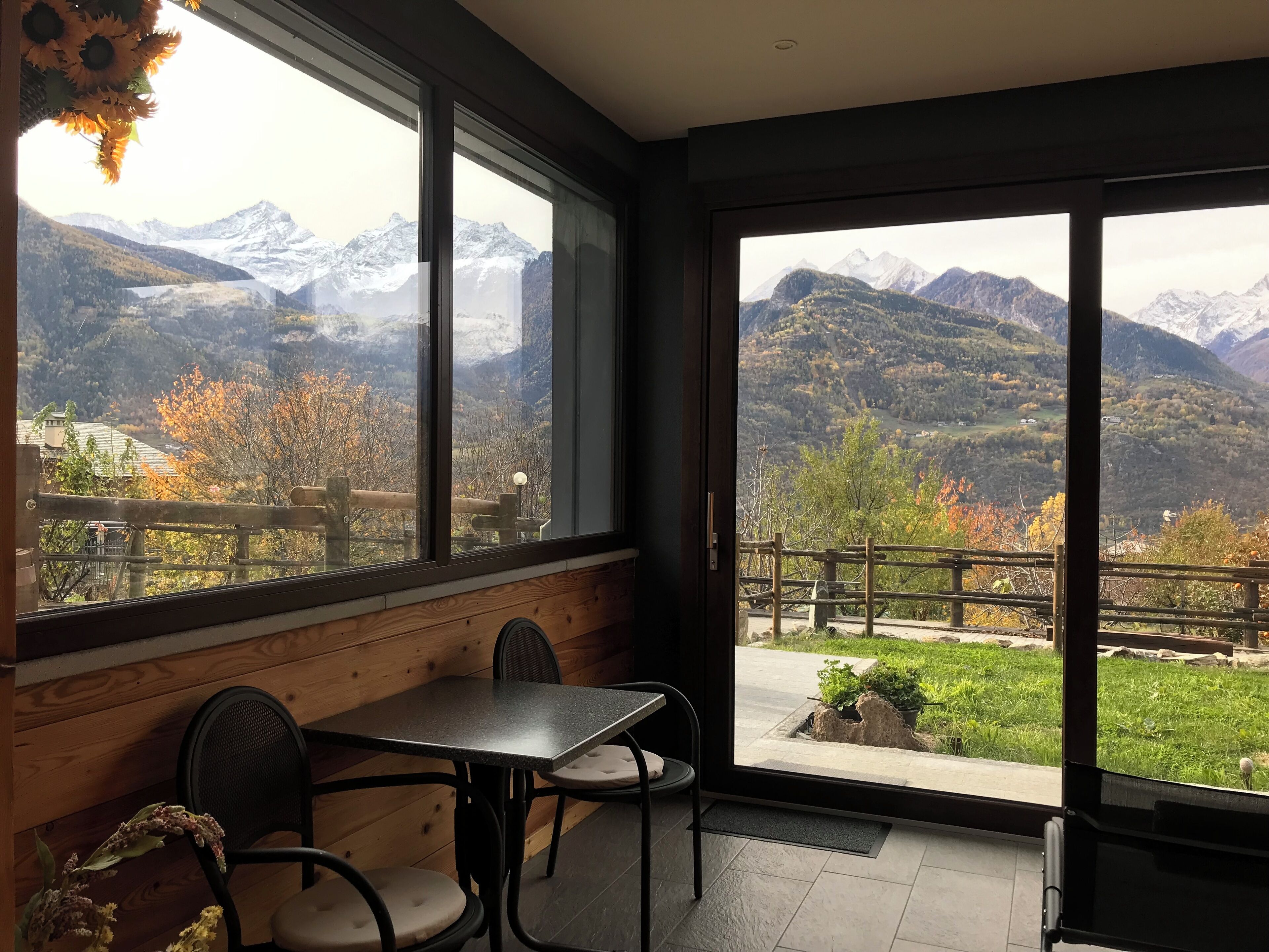 A room with a view of mountains, a wooden bench, and a table with chairs.