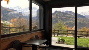 A room with a view of mountains, a wooden bench, and a table with chairs.