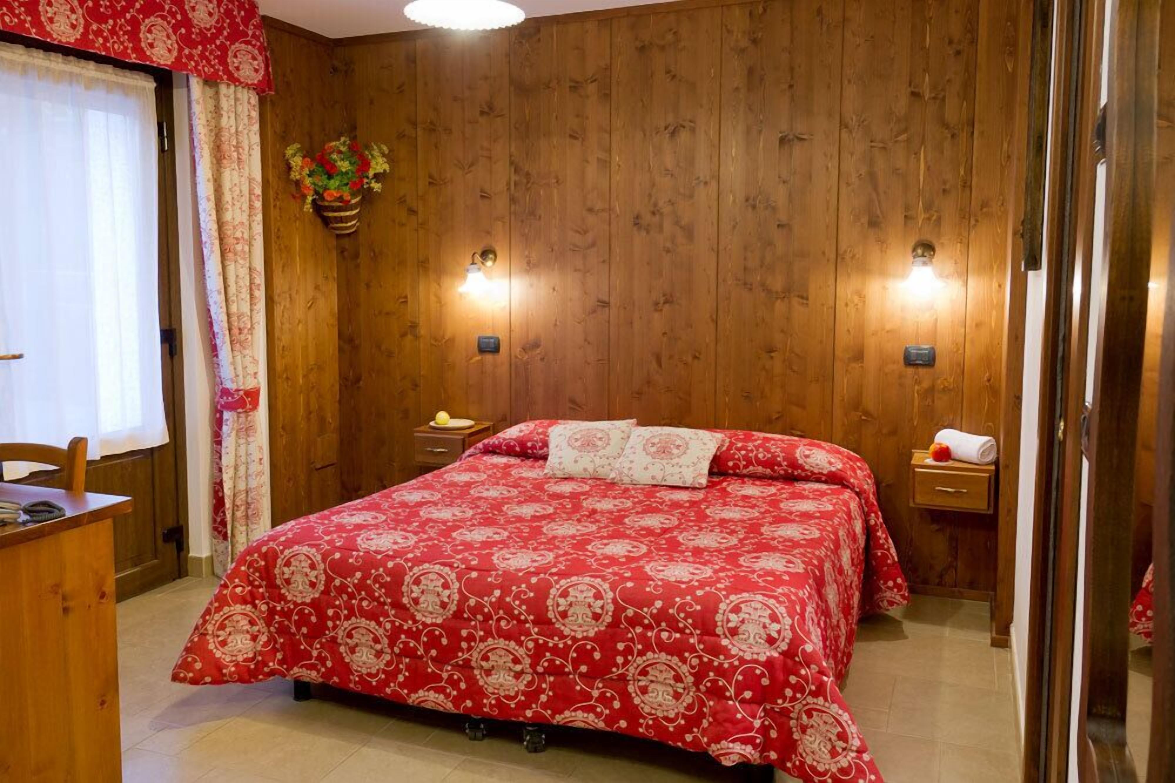 A wooden-paneled bedroom with a large bed, two bedside tables, and a small desk.
