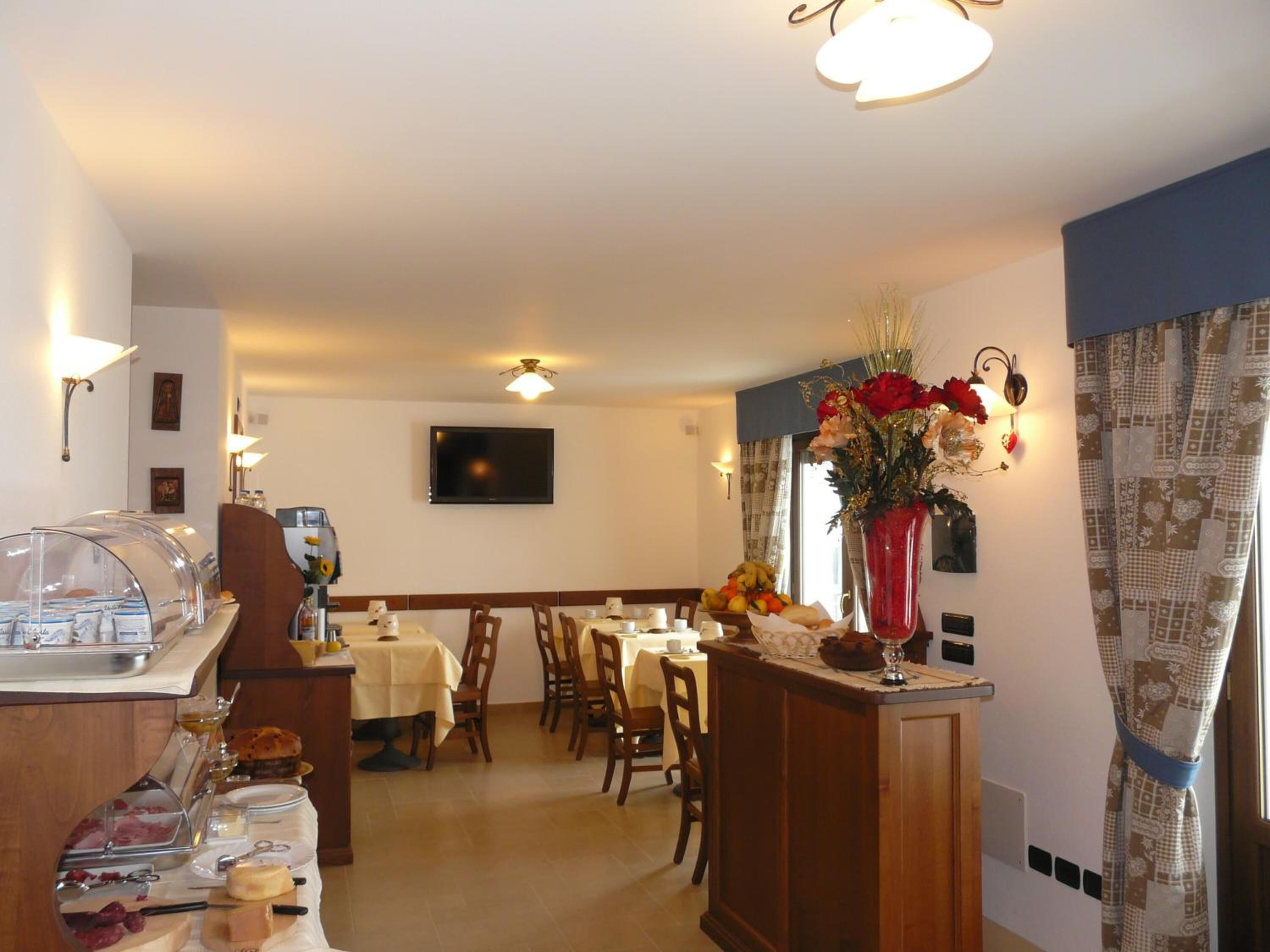A hotel dining area with tables, chairs, a buffet, and a TV on the wall.
