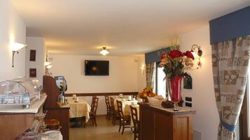 A hotel dining area with tables, chairs, a buffet, and a TV on the wall.