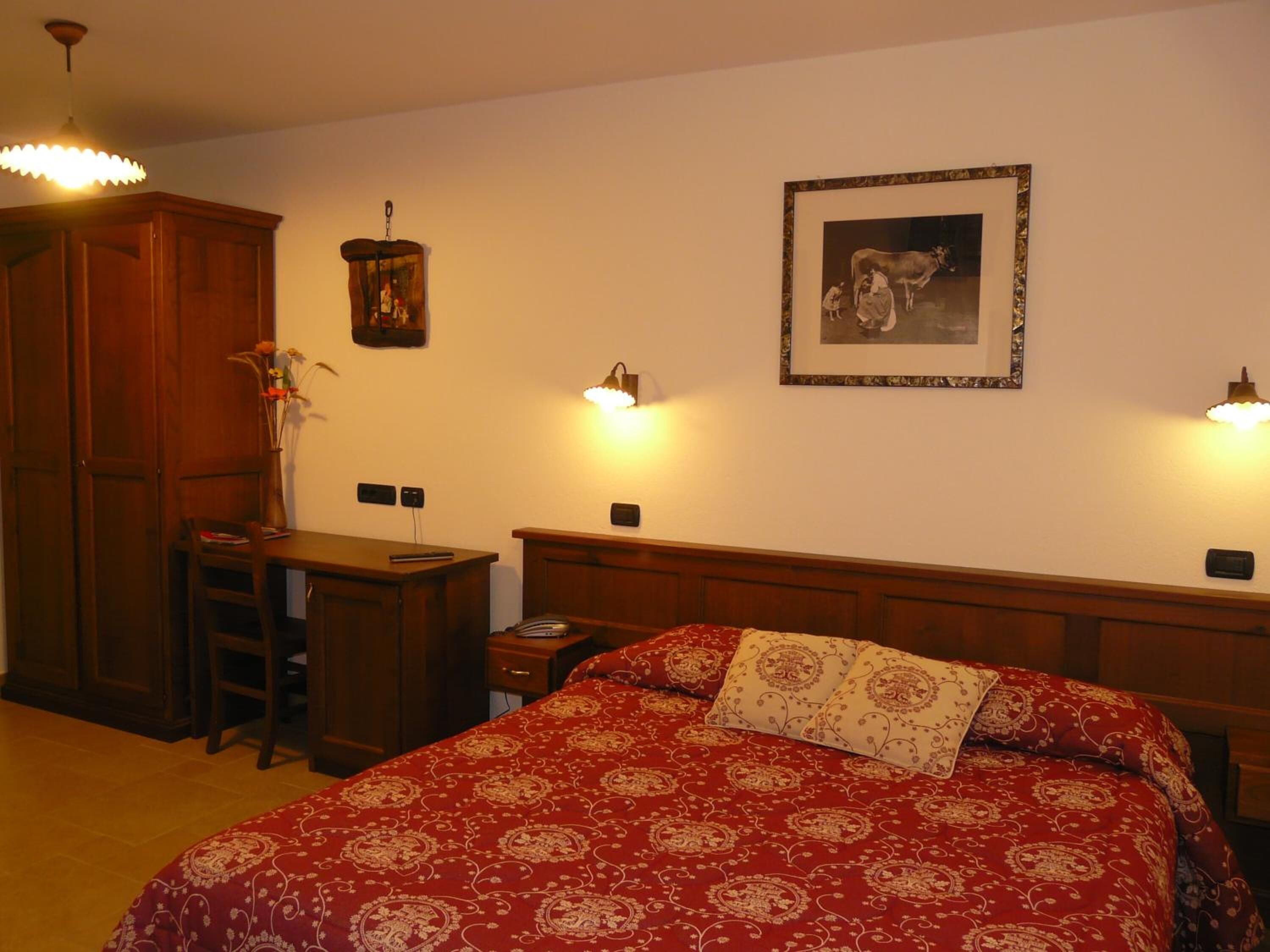Un dormitorio con cama de madera, un escritorio y una silla. Hay un cuadro en la pared y una lámpara colgante.