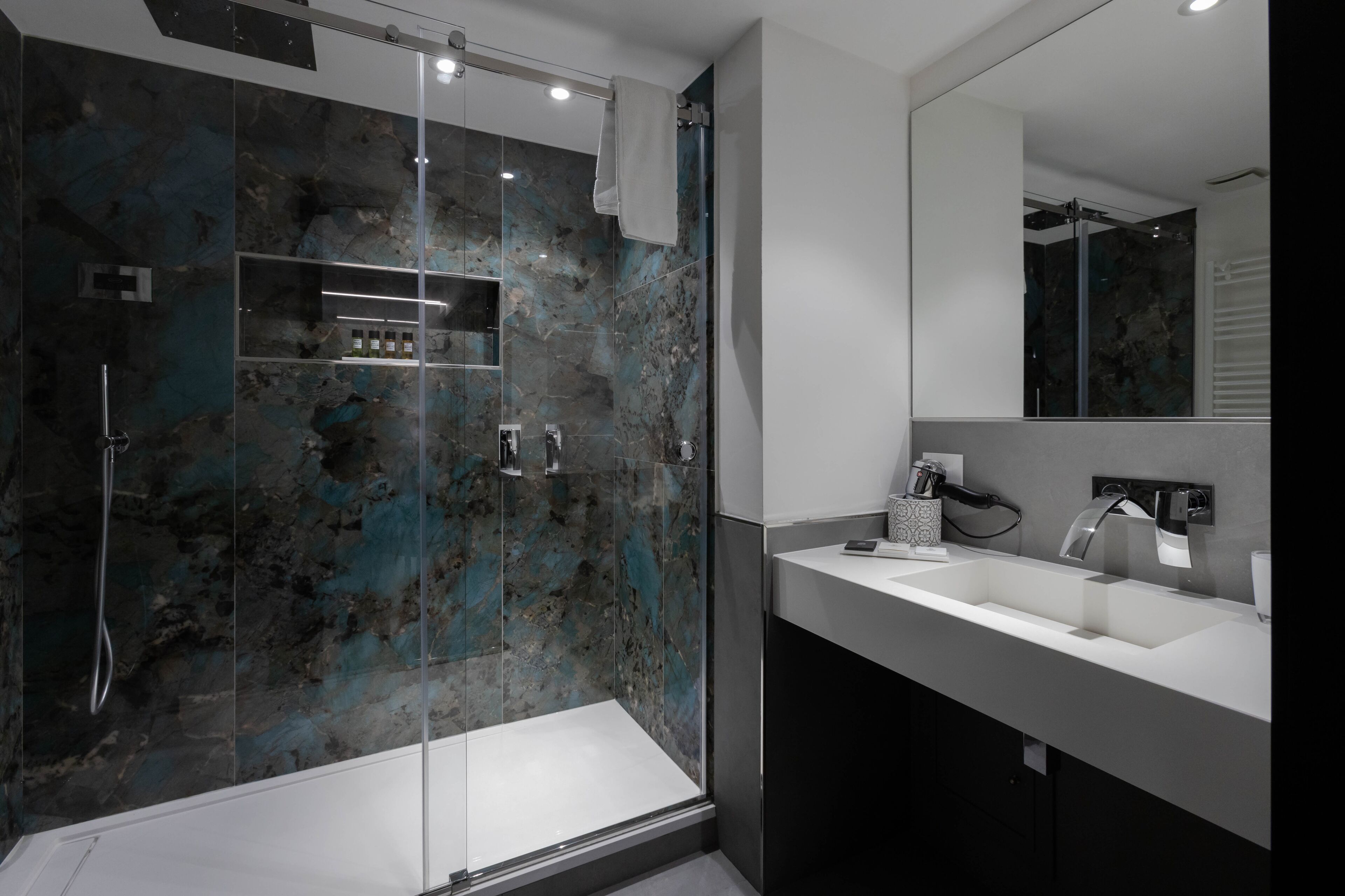 A modern bathroom with a glass-enclosed shower, marble walls, and a white vanity with a large mirror.