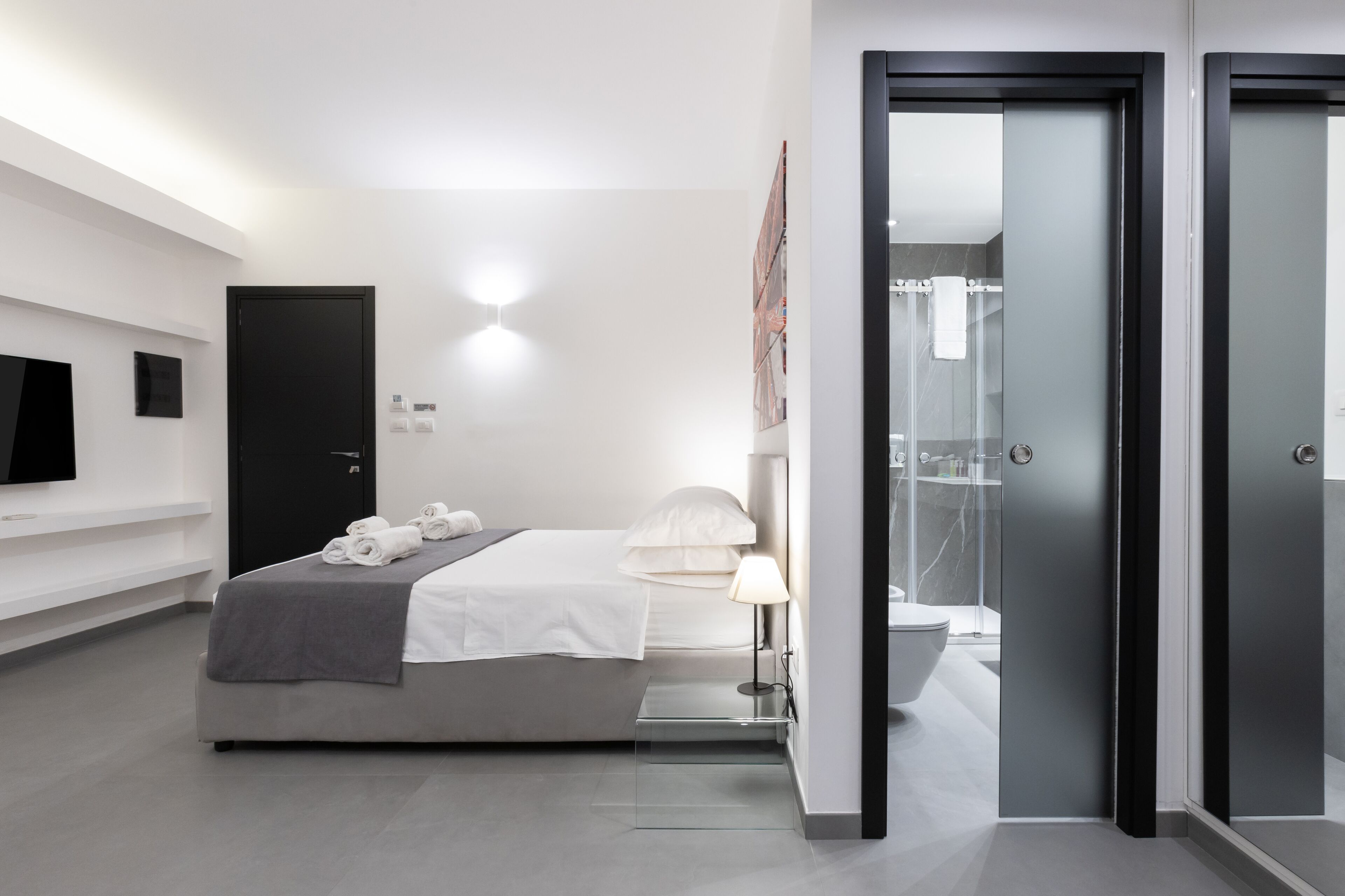 Une chambre d'hôtel moderne équipée d'un lit, d'une lampe de chevet et d'une cabine de douche en verre.
