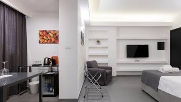 Een moderne hotelkamer met een bed, een televisie, een bank, een bureau met een waterkoker, en een klein plankje met een plant.