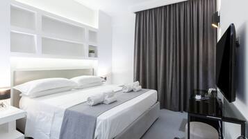 A modern hotel room with a neatly made bed, a flat-screen TV, a desk with a chair, and a large window with curtains.