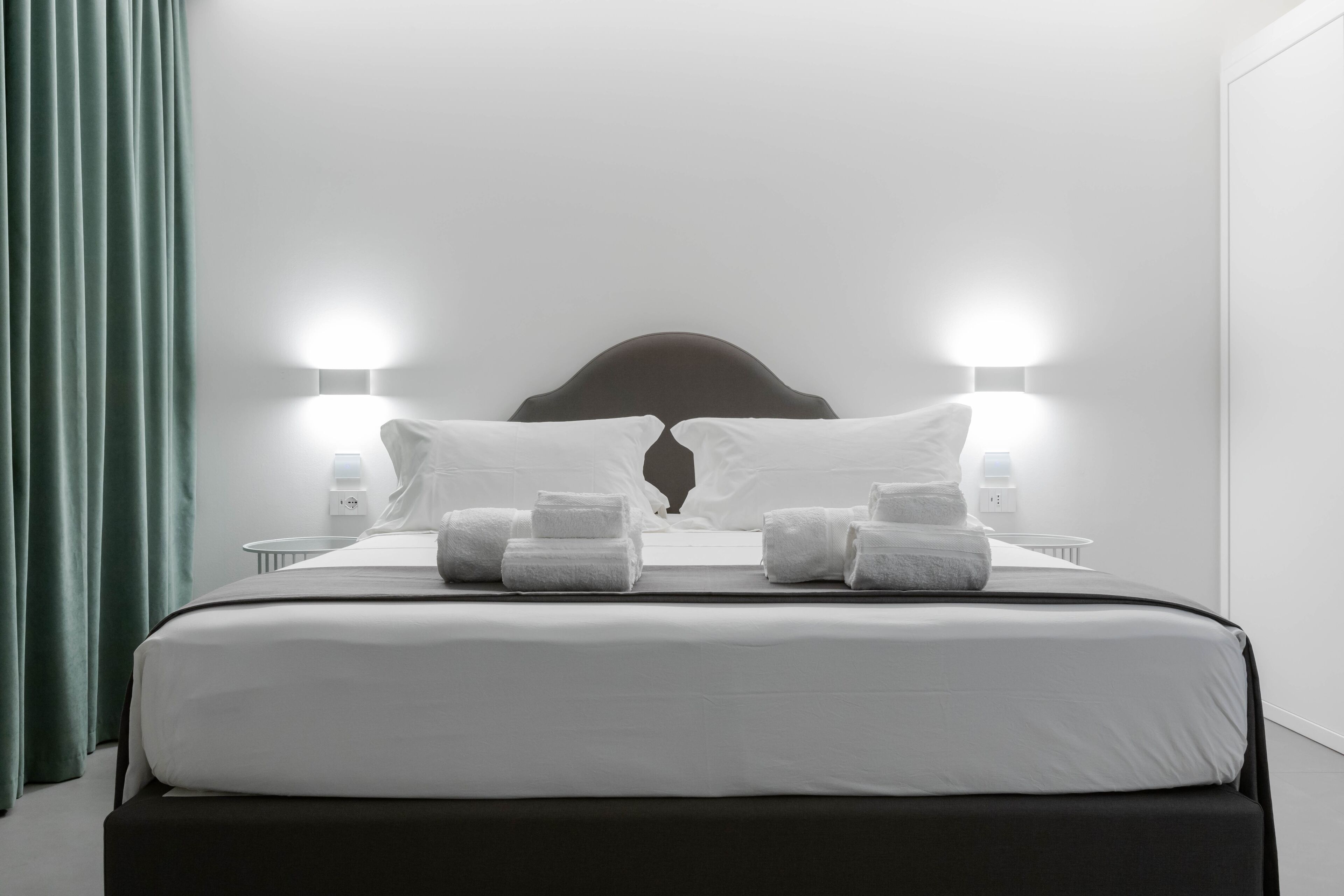 A neatly made bed with white linens and two pillows, flanked by two bedside lamps.