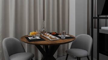 Una mesa de comedor redonda con tapa de madera, dos sillas grises tapizadas y una bandeja rectangular blanca con pasteles y fruta.