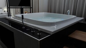 A modern bathroom with a large bathtub, a mirror, and wooden flooring. - Suite Palermo Apartment (Palermo)