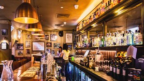 Una zona de bar con una barra larga, varias luces colgantes y estantes llenos de botellas.