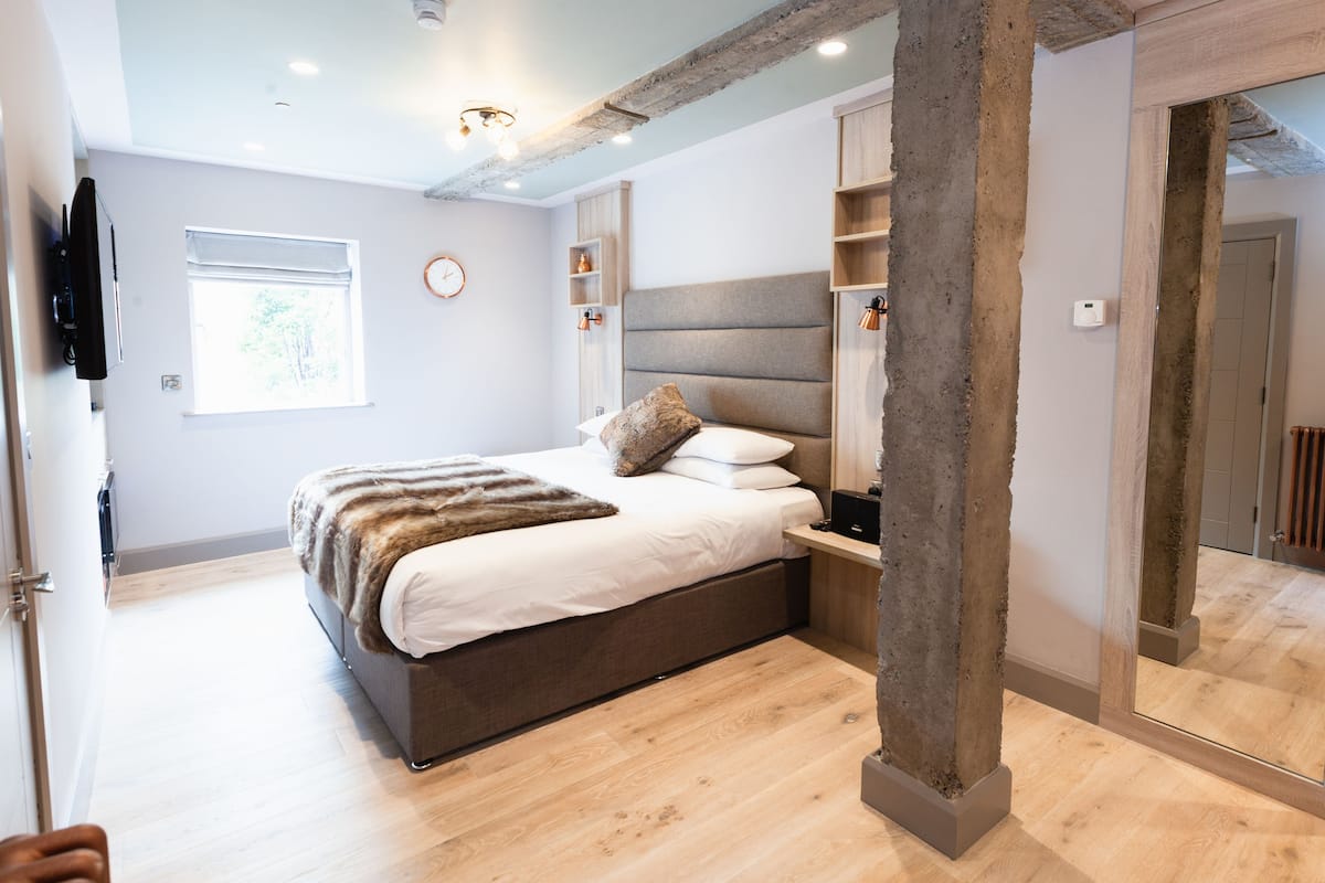 A modern bedroom with a large bed, wooden flooring, and a concrete pillar.