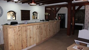 Een receptiezone met een houten receptiebalie, een computer en een stoel. Er staan decoratieve vazen aan de muur en er is behang met een patroon aan de rechterkant.