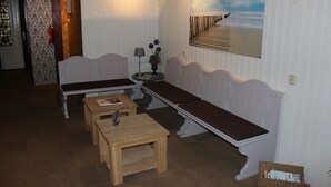 Een kamer met een lange bank, een klein tafeltje en een aan de muur hangend schilderij van een strand.