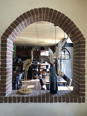 Un arco de ladrillo que da paso a un comedor con mesas y sillas, una lámpara colgante y plantas decorativas.