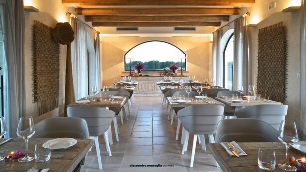 A restaurant with a long table layout, wooden beams, and a view through an arched window. - Le Scuderie - Castello Monaci (Salice Salentino)