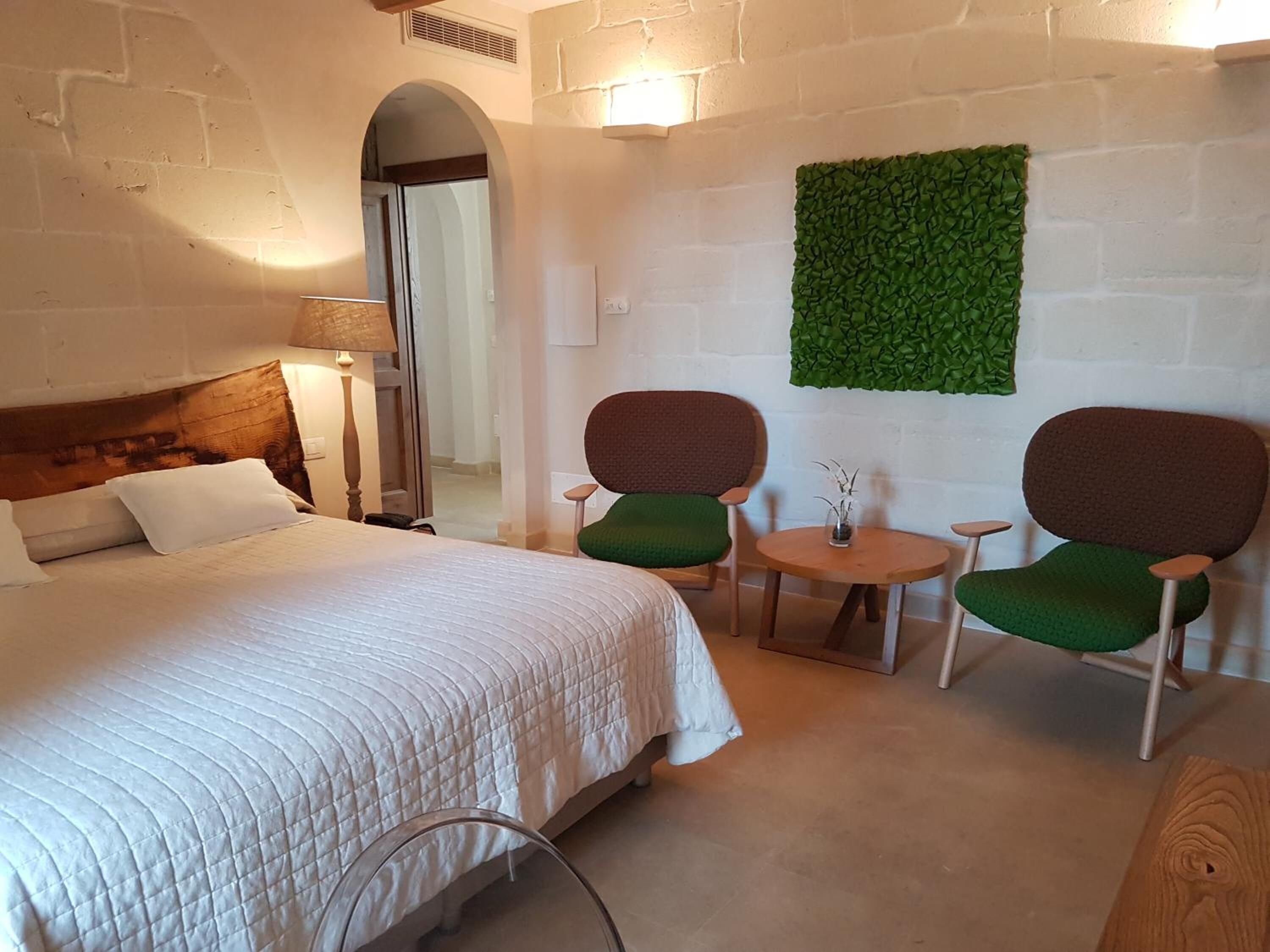 Ett hotellrum med en säng, två stolar, ett litet bord och en grön väggdekoration.