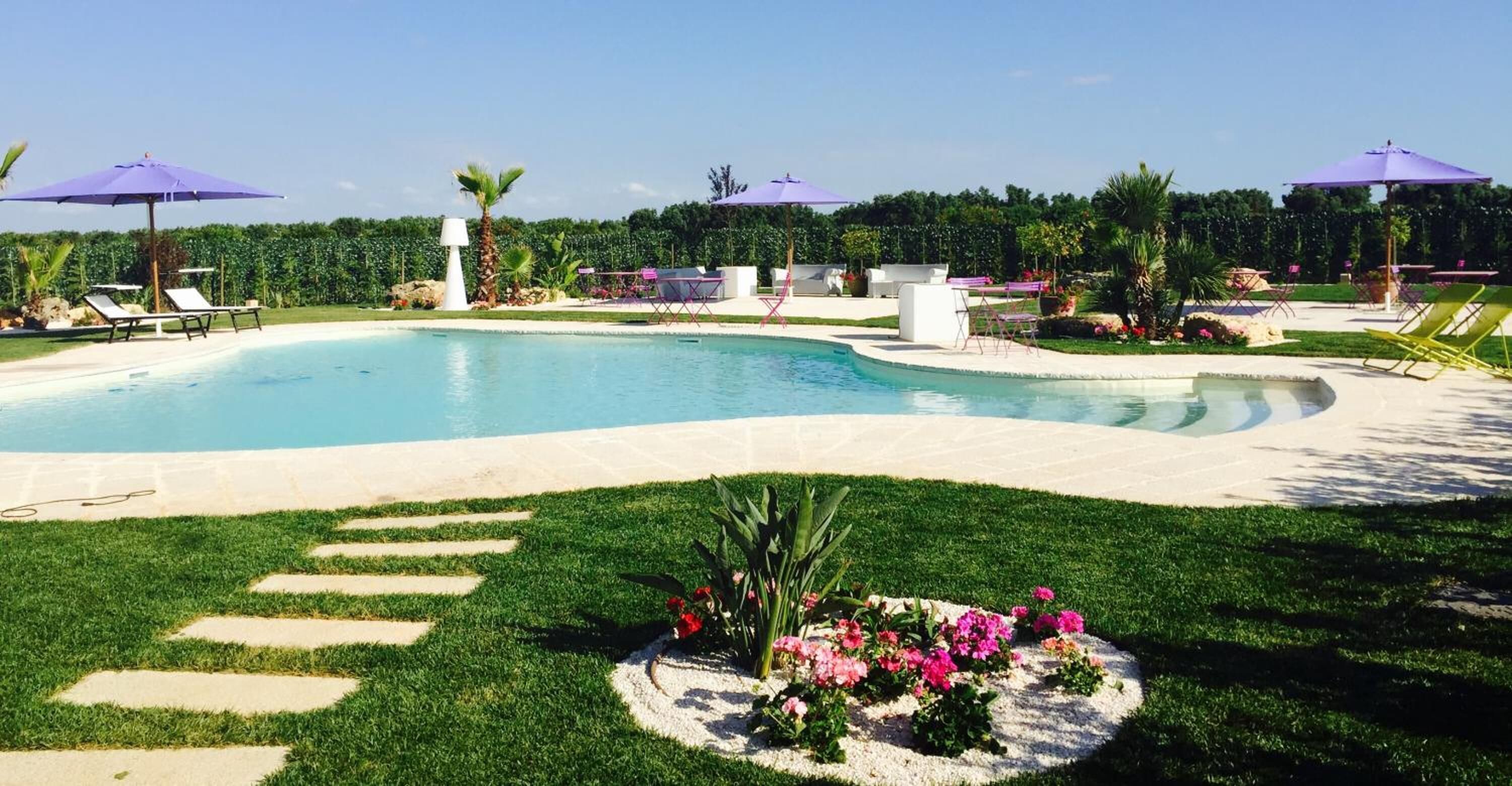 A swimming pool with lounge chairs and umbrellas, surrounded by well-manicured grass and flowers.