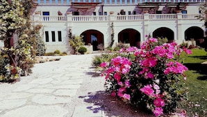 A courtyard with a stone pathway leading to a building with arched doorways and a white facade. - Le Scuderie - Castello Monaci (Salice Salentino)
