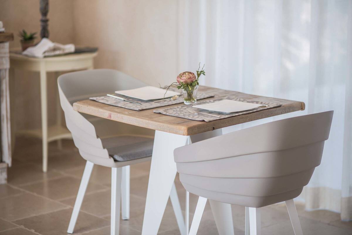 A dining table with two chairs, a vase with a single flower, and a small table with a plant and a folded cloth.