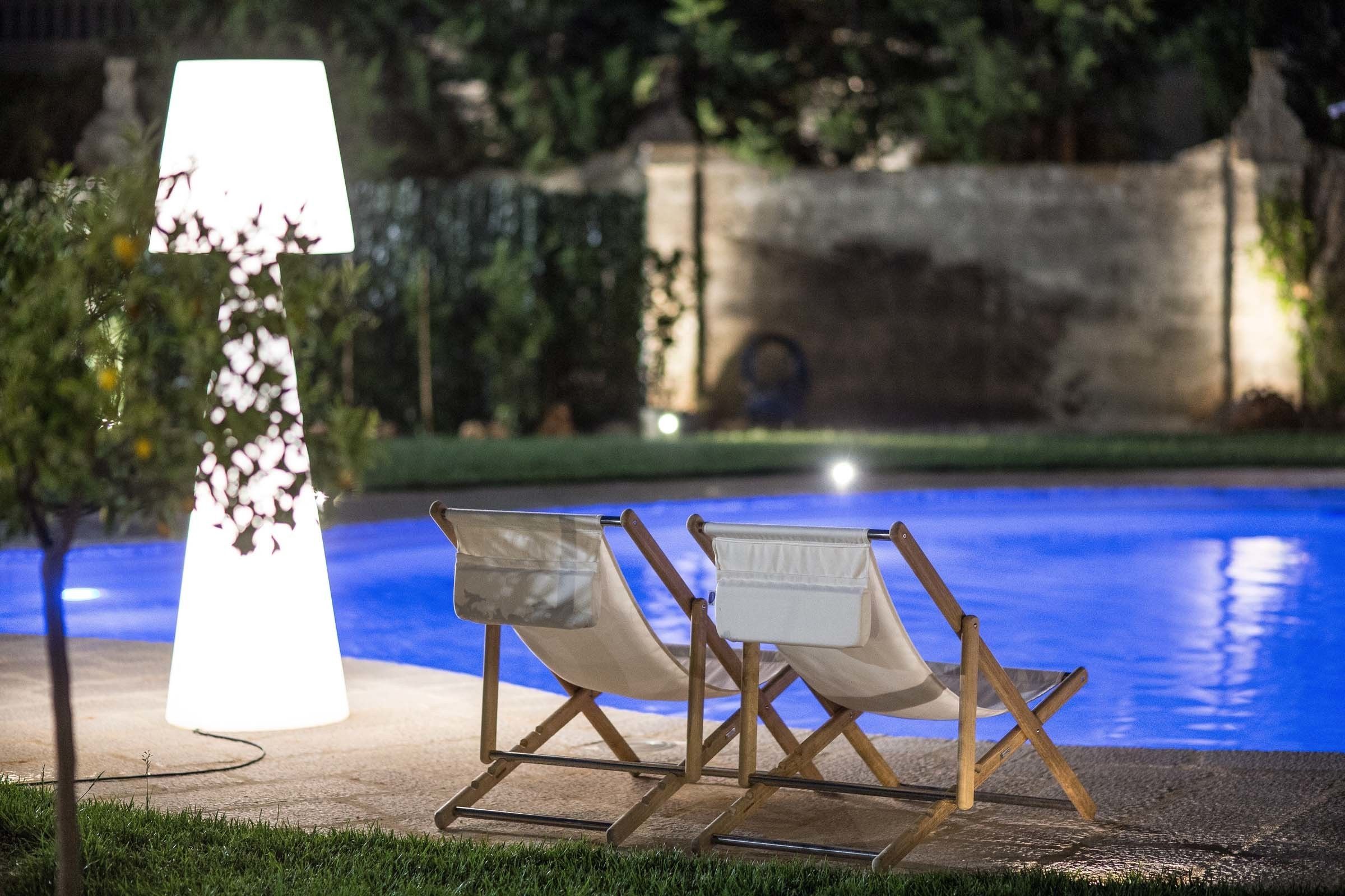 Dos sillones de relax junto a una piscina, con una lámpara y flores.