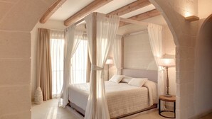 A bedroom with a four-poster bed, stone walls, and a wooden ceiling beam. - Le Scuderie - Castello Monaci (Salice Salentino)