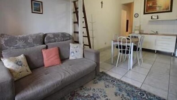 Un salon avec un canapé gris, un tapis à motifs et un coin repas comprenant une table et des chaises blanches.