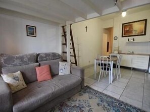 Un salon avec un canapé gris, un tapis à motifs et un coin repas comprenant une table et des chaises blanches.