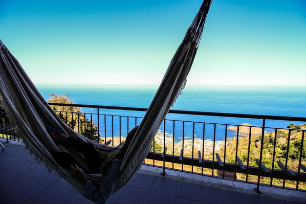 A hammock on a balcony overlooking a coastal view.