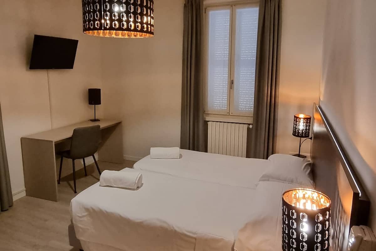 Habitación de hotel con cama, escritorio, silla y dos lámparas de noche.