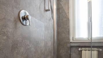 A modern bathroom with a shower, a glass-enclosed shower area, and a window providing natural light.