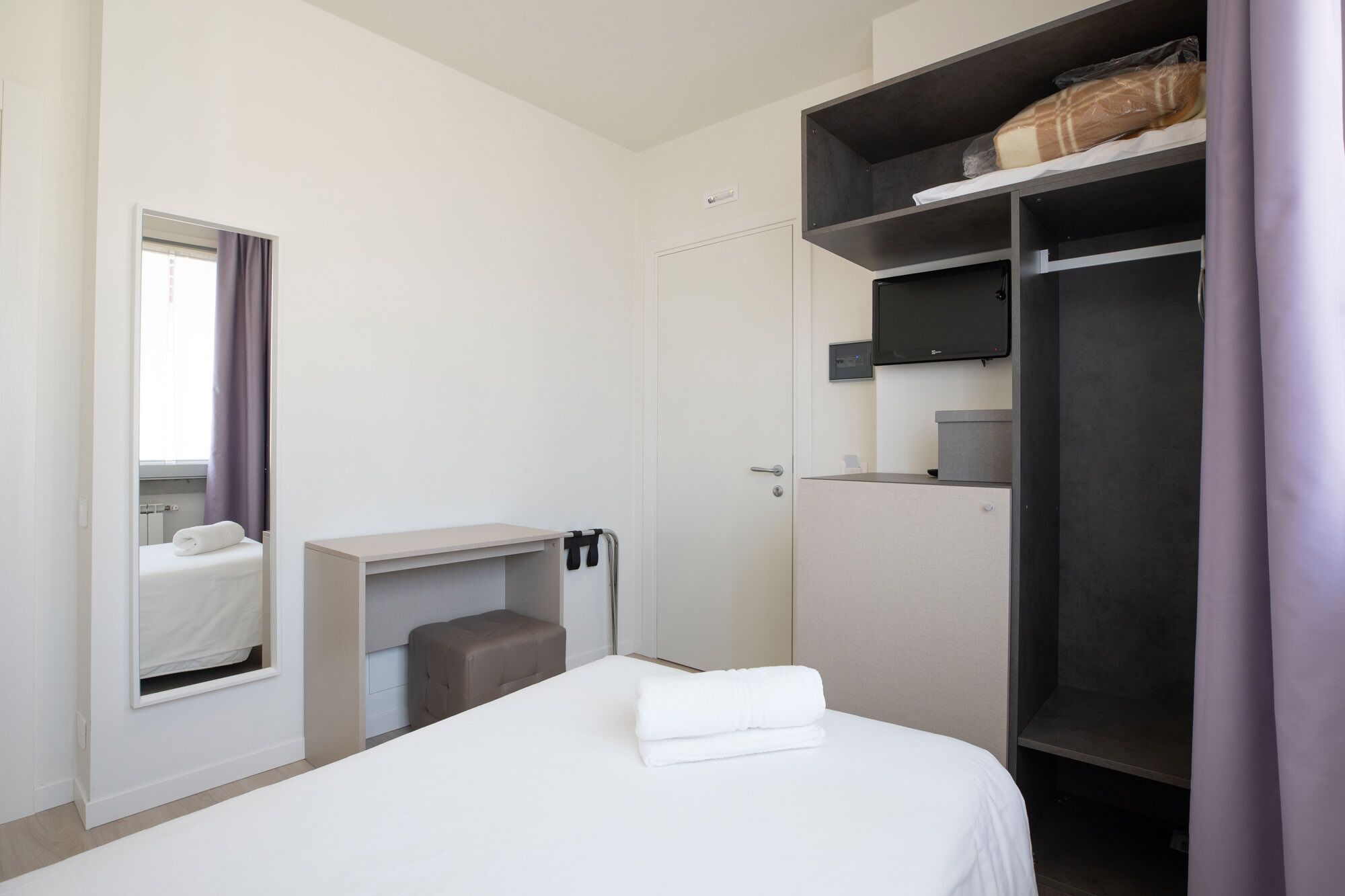 A hotel room with a bed, a desk, a wardrobe, and a bathroom.