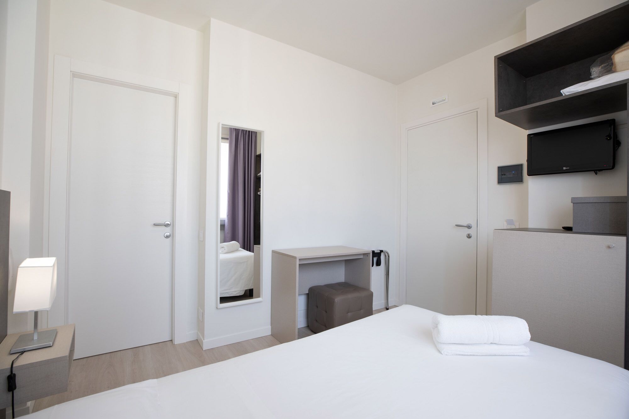 A hotel room with a bed, a desk, a chair, a TV, and a wardrobe.