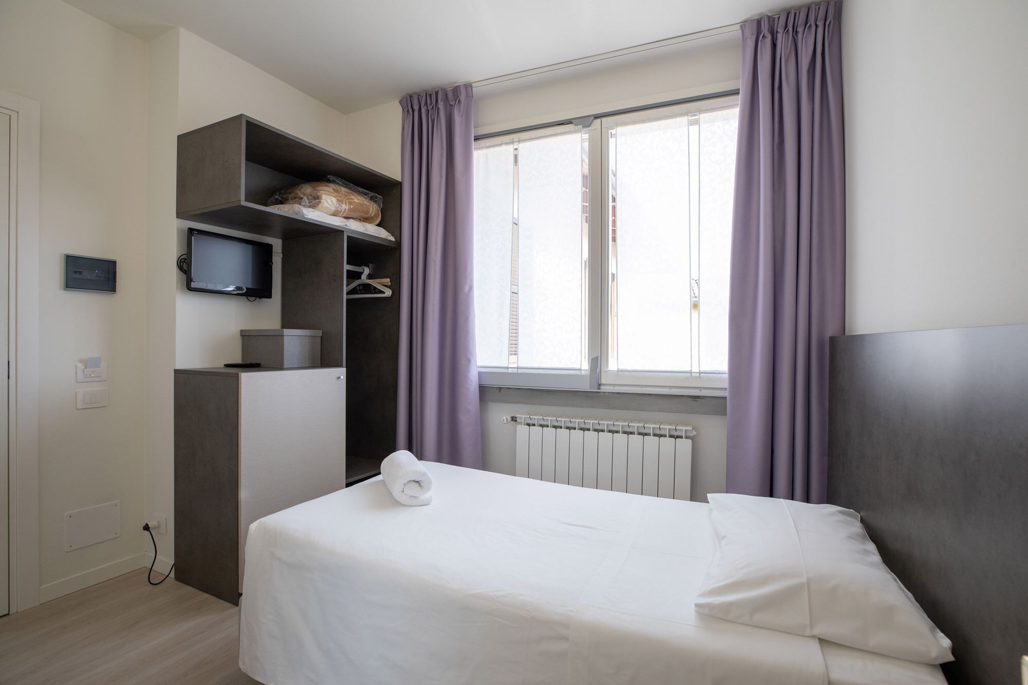 Une chambre d’hôtel avec un lit, une télévision, une armoire et une fenêtre avec des rideaux.