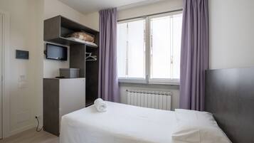 Une chambre d’hôtel avec un lit, une télévision, une armoire et une fenêtre avec des rideaux.