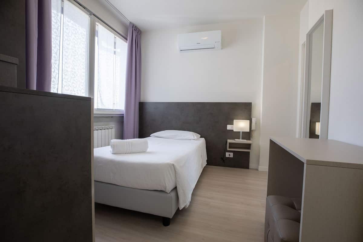 Una habitación de hotel con cama, escritorio, lámpara y ventana con cortinas.