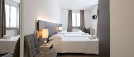 A hotel room with two beds, a chair, a desk with a lamp, a flat-screen TV, and a large mirror.