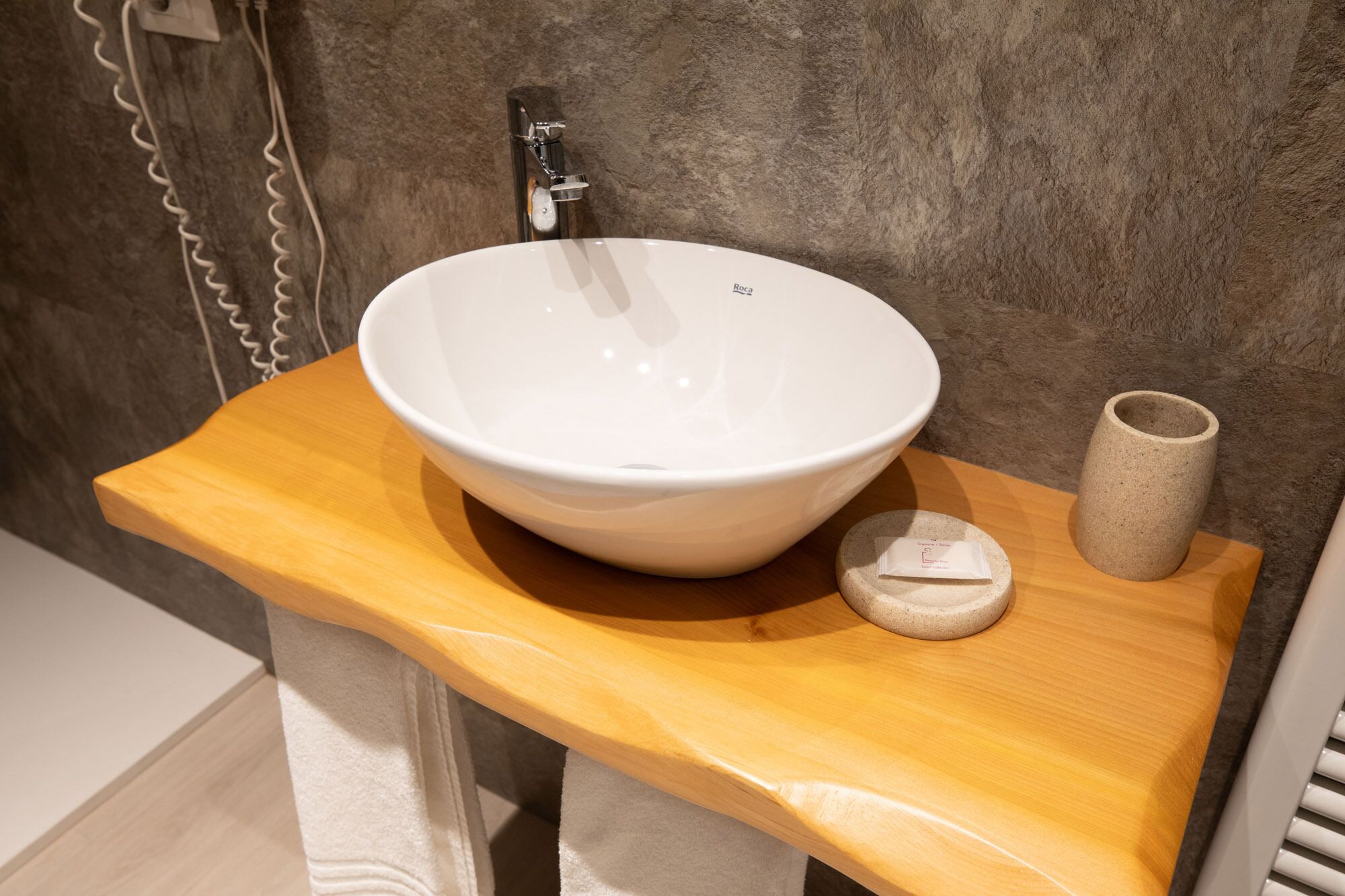 Un baño con un lavabo de cerámica blanca, un mueble de tocador de madera y un jarrón beige.