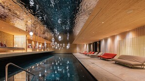 An indoor swimming pool with a wooden ceiling, lounge chairs, and a glass barrier. - Anewandter Historic Hotel (Gais)