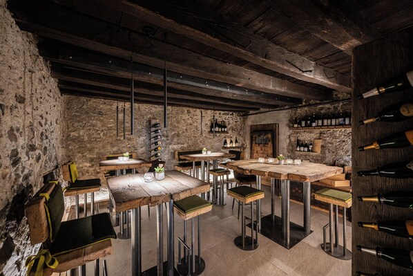 A rustic interior with exposed stone walls, wooden tables, and metal bar stools. - Anewandter Historic Hotel (Gais)
