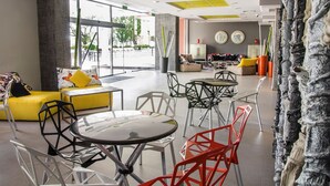 A modern lobby with a yellow sofa, round tables, and colorful chairs. - Gladiola Star (Golden Sands)