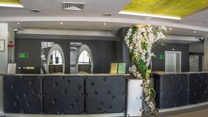 A reception area with a black tufted desk, a large mirror, and a floral arrangement. - Gladiola Star (Golden Sands)